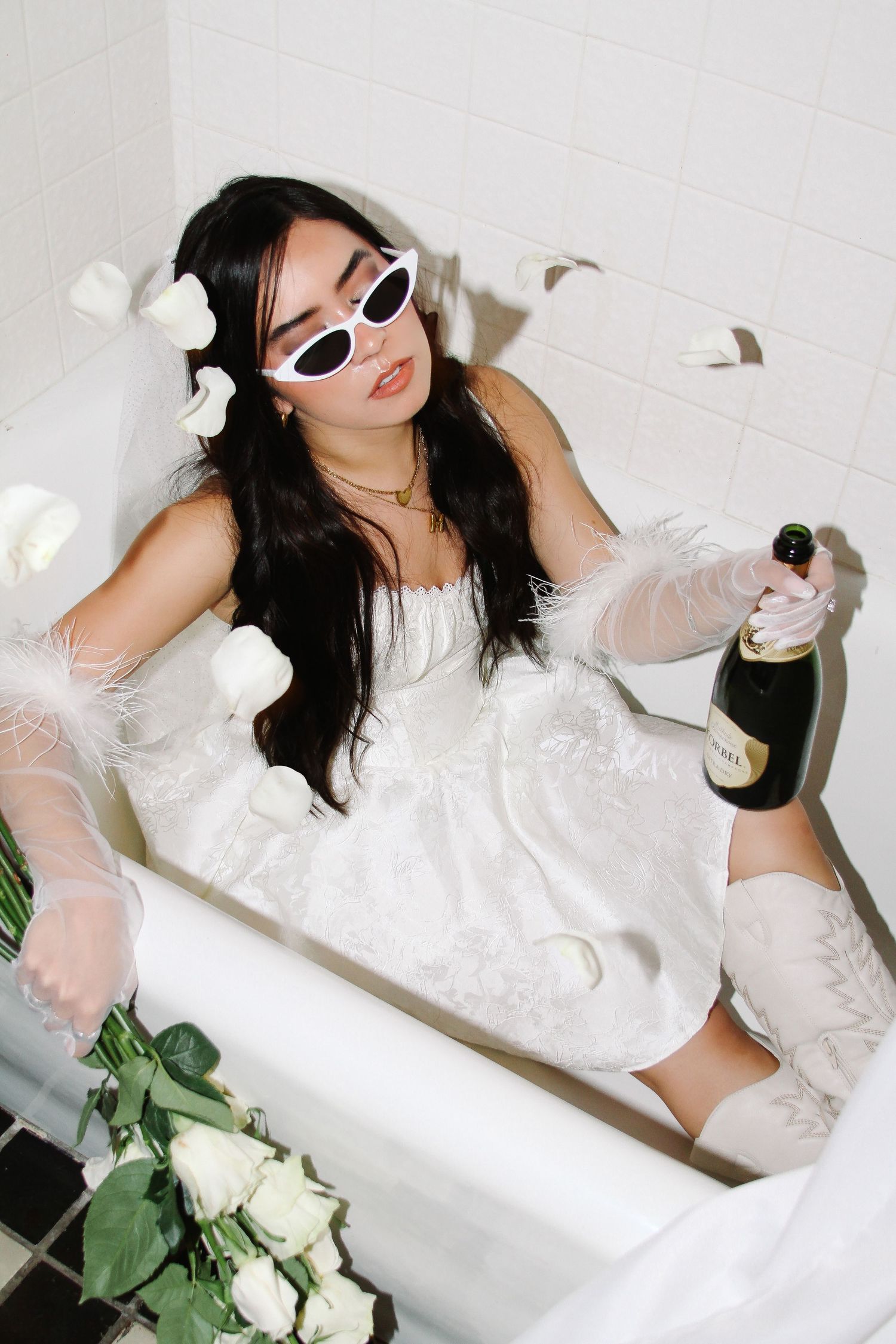 Creative bathtub portrait with white dress, sunglasses and champagne bottle styling.