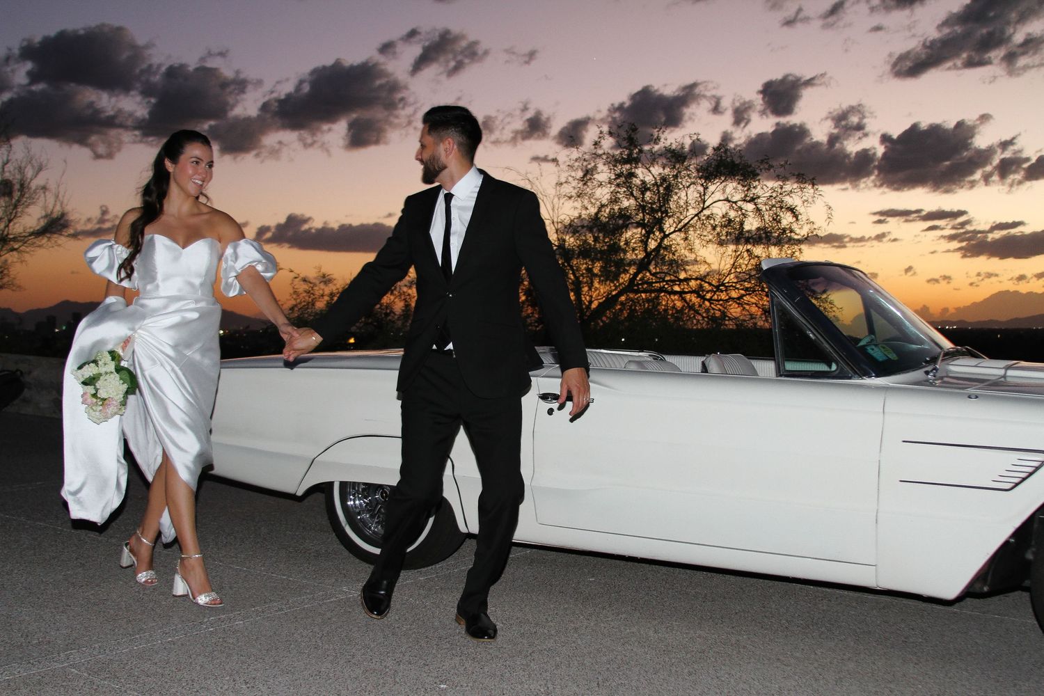 Wedding couple walking near white limousine during sunset.