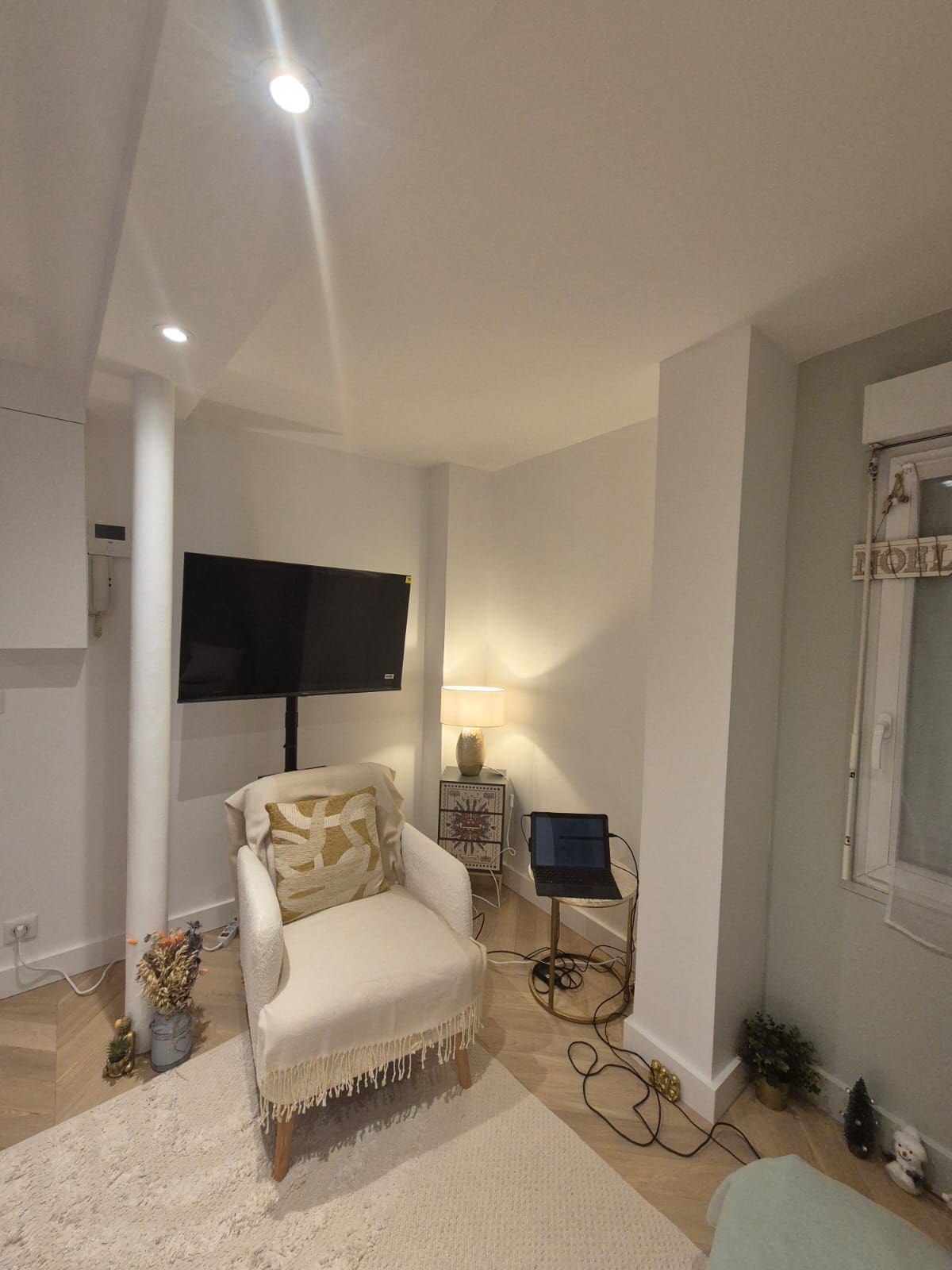 Modern basement living space with white armchair, wall-mounted TV, and cozy decor including throw pillows and carpet.