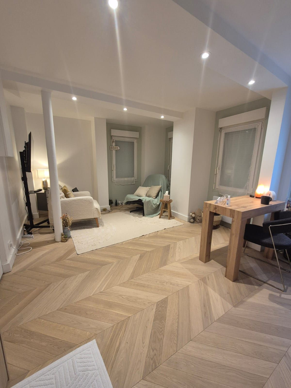 Modern living room with herringbone wood floors, recessed lighting, and minimalist furniture in neutral tones.