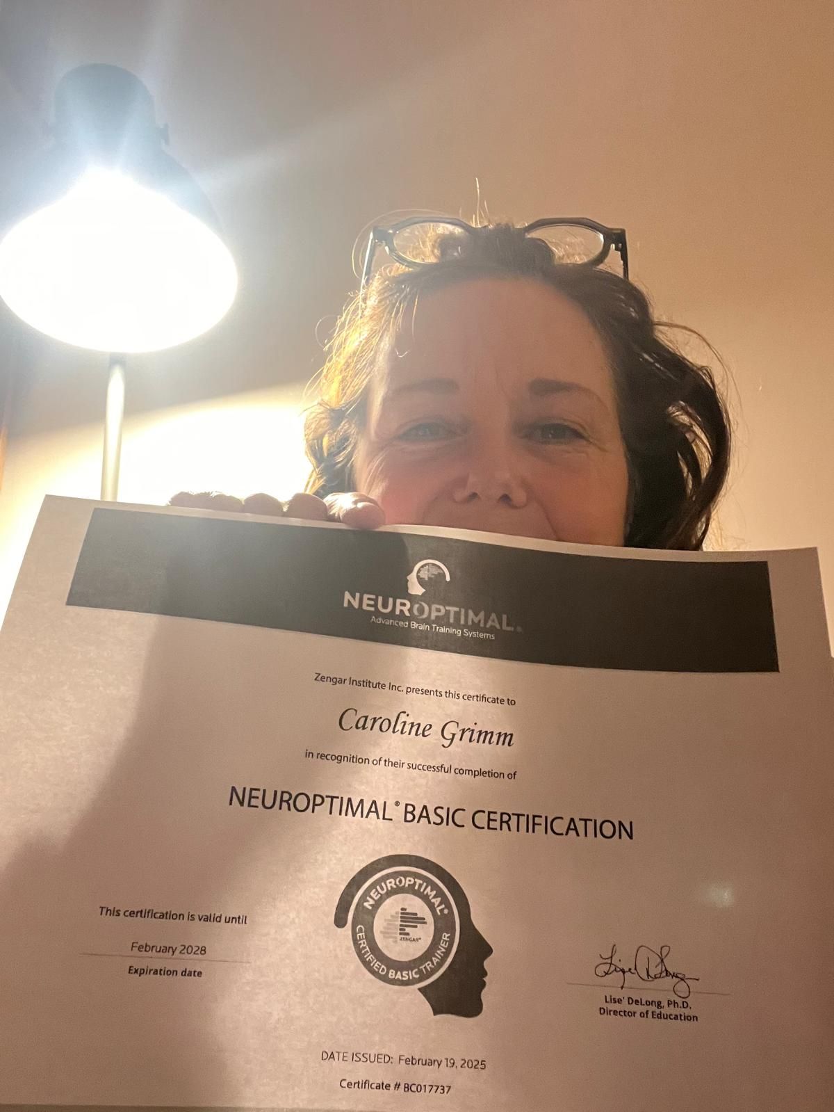Person holding up a NeuroOptimal Basic Certification document with ceiling light in background.
