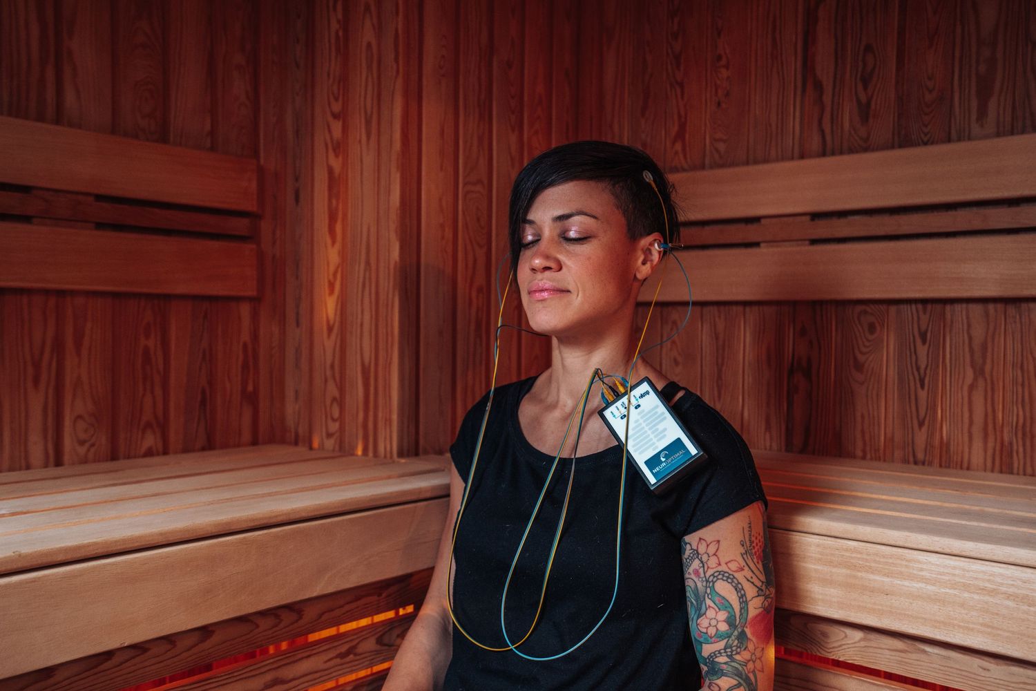 Person relaxing in wooden sauna while wearing headphones and casual attire.