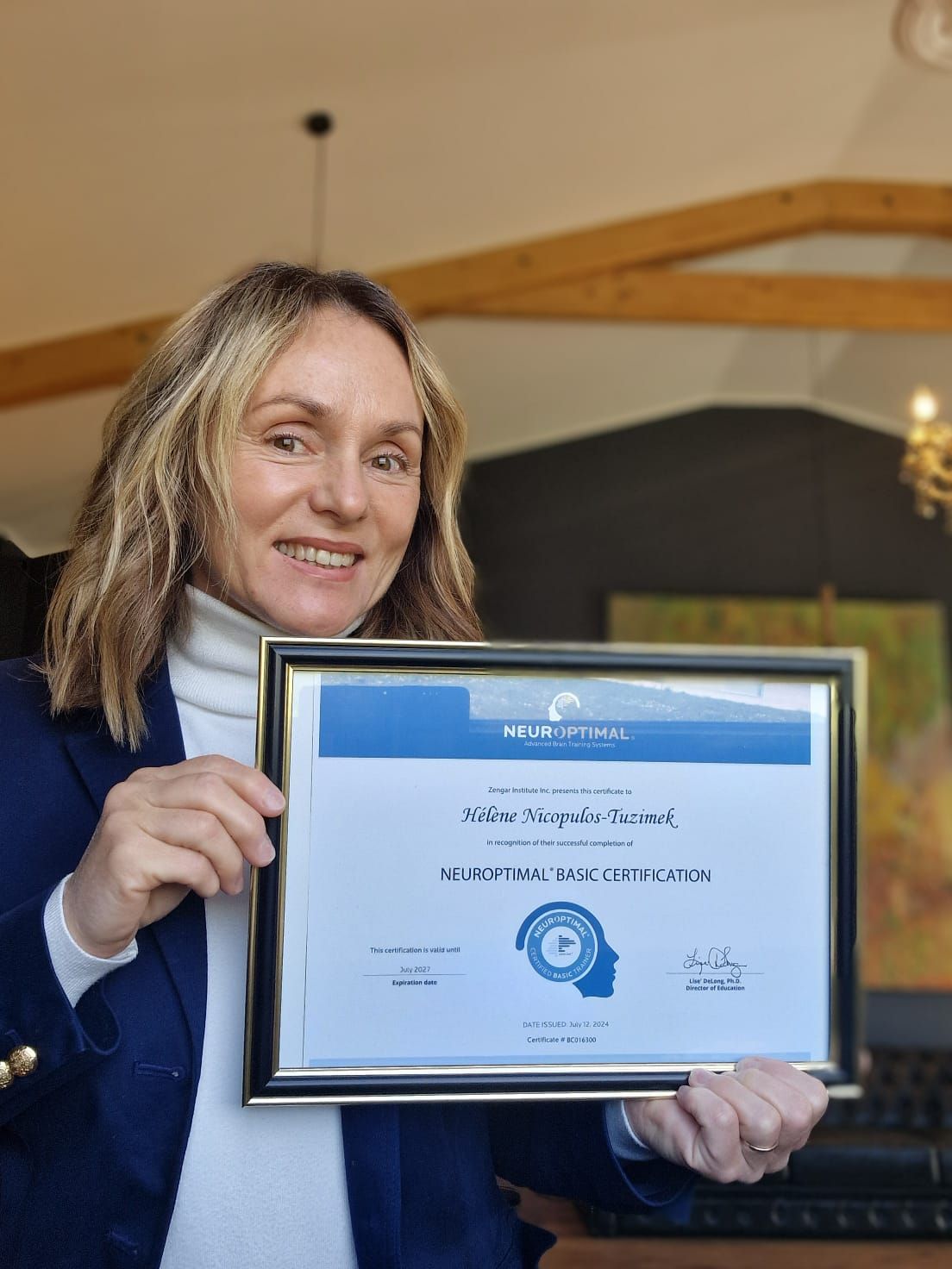 Individual displaying NeuroOptimal certification in navy blazer against wooden wall decor.
