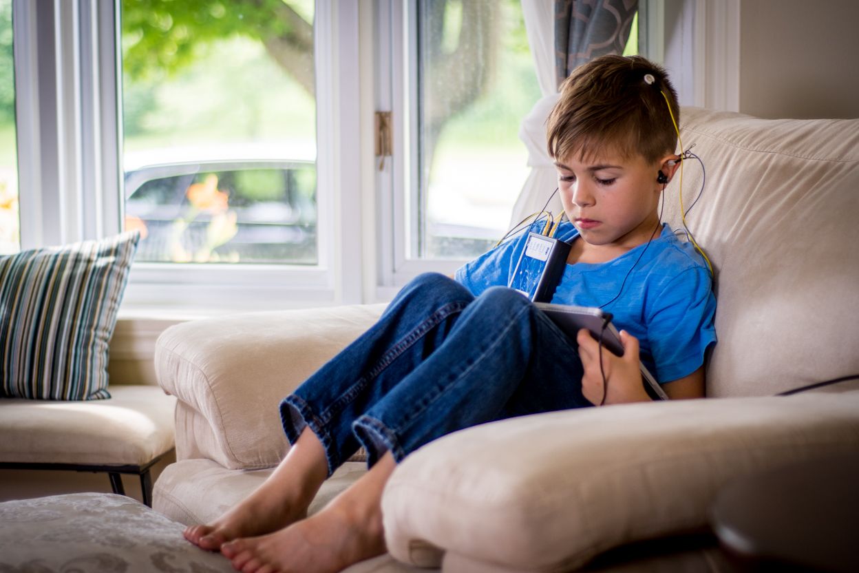 Young child relaxing on couch using digital device in casual home setting.