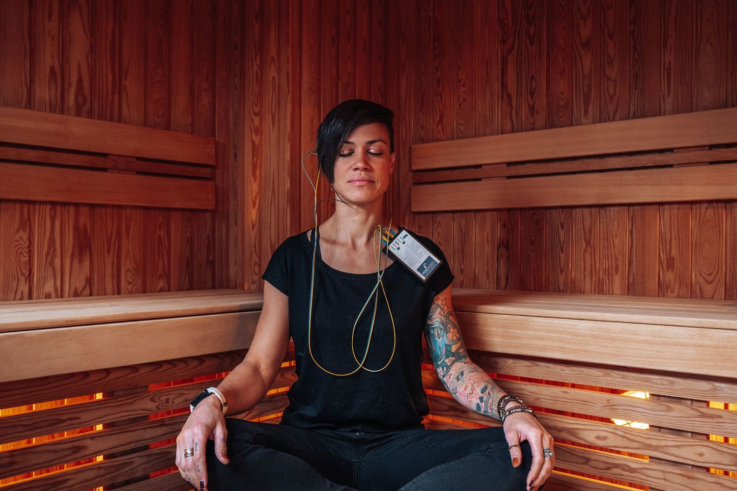 Someone meditates in a relaxing sauna while wearing a black t-shirt, with headphones and a mobile phone attached.