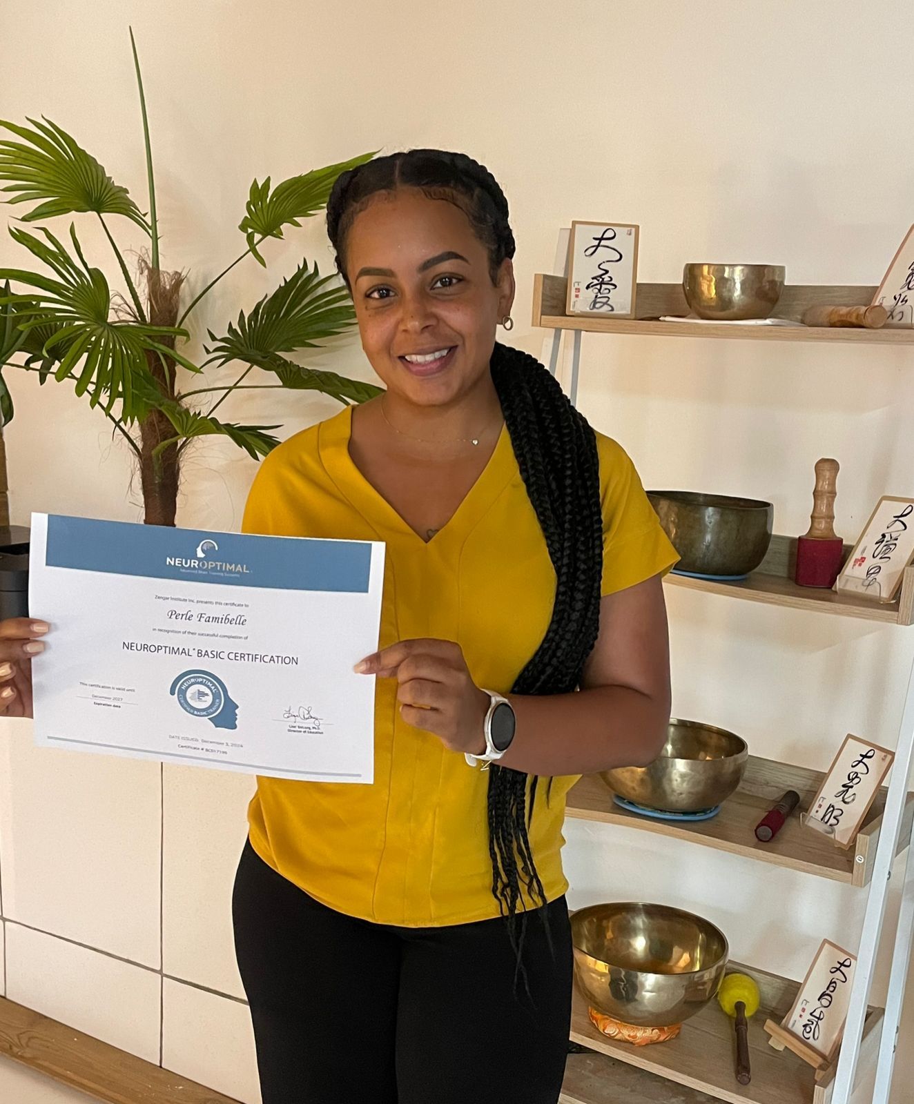 Person in yellow top displaying certification in room with Asian decor and singing bowls.