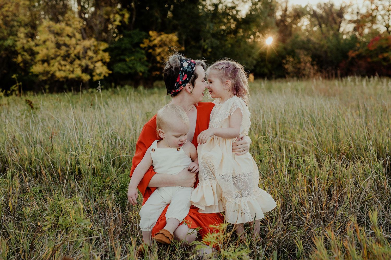 Beautiful sunset family photo in a golden field with mother and two children wearing red and white dresses.