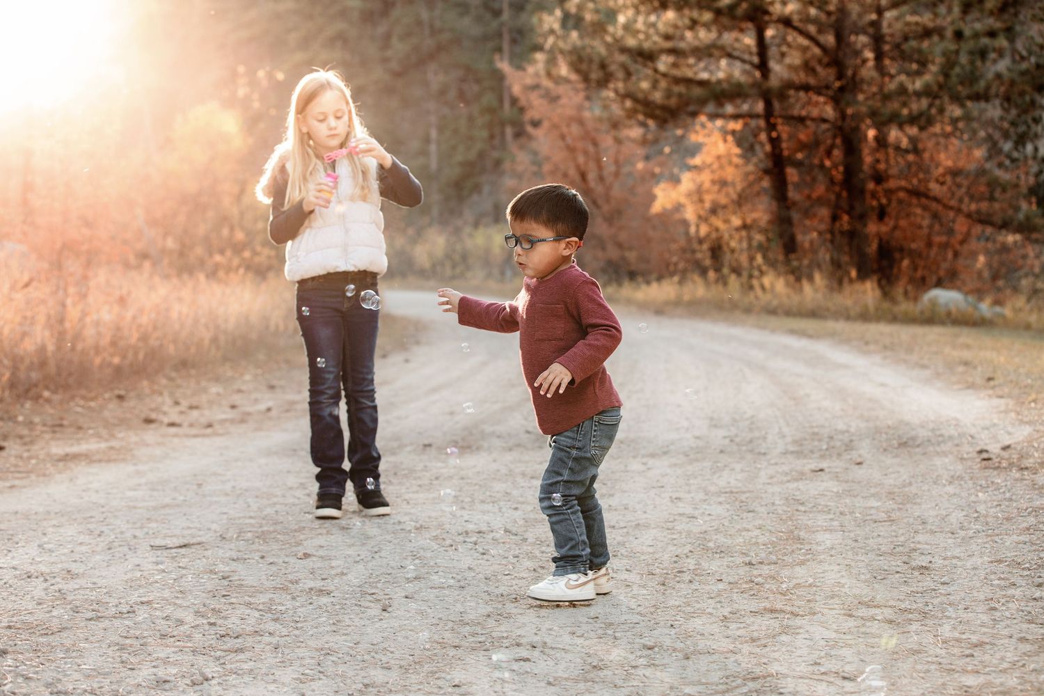 Two children play together on a gravel path during golden hour in an autumn setting.
