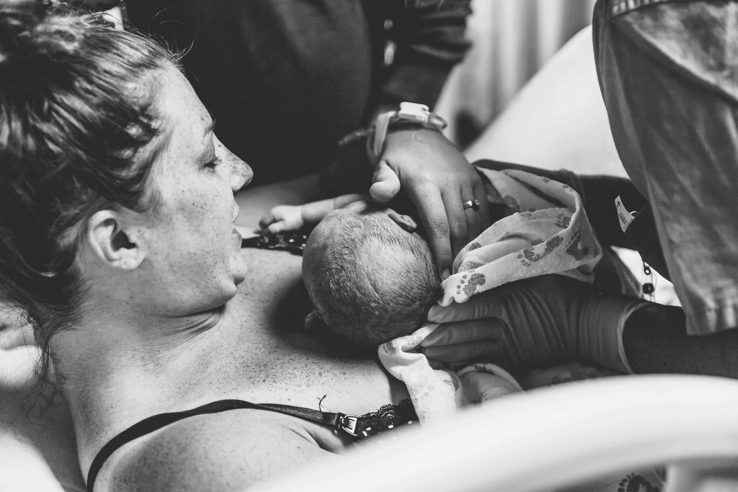 A black and white photograph shows immediate skin-to-skin contact after birth in a medical setting.