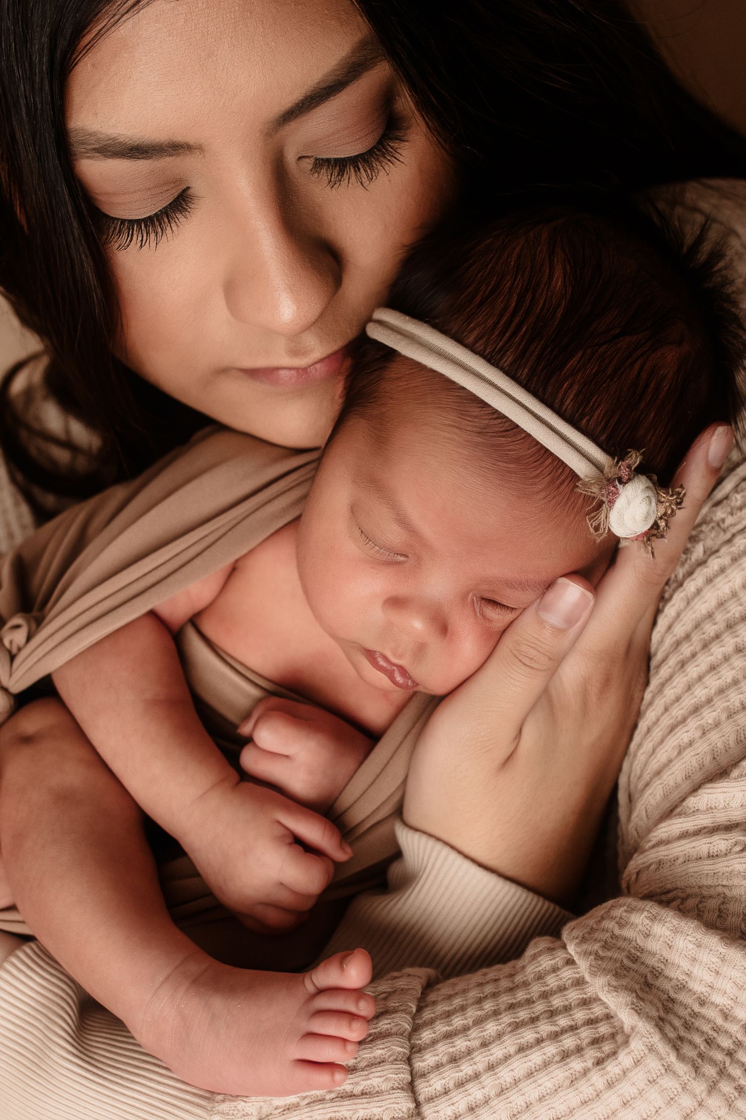 A tender moment as parent and newborn baby share a peaceful embrace in soft beige tones during an intimate portrait session.