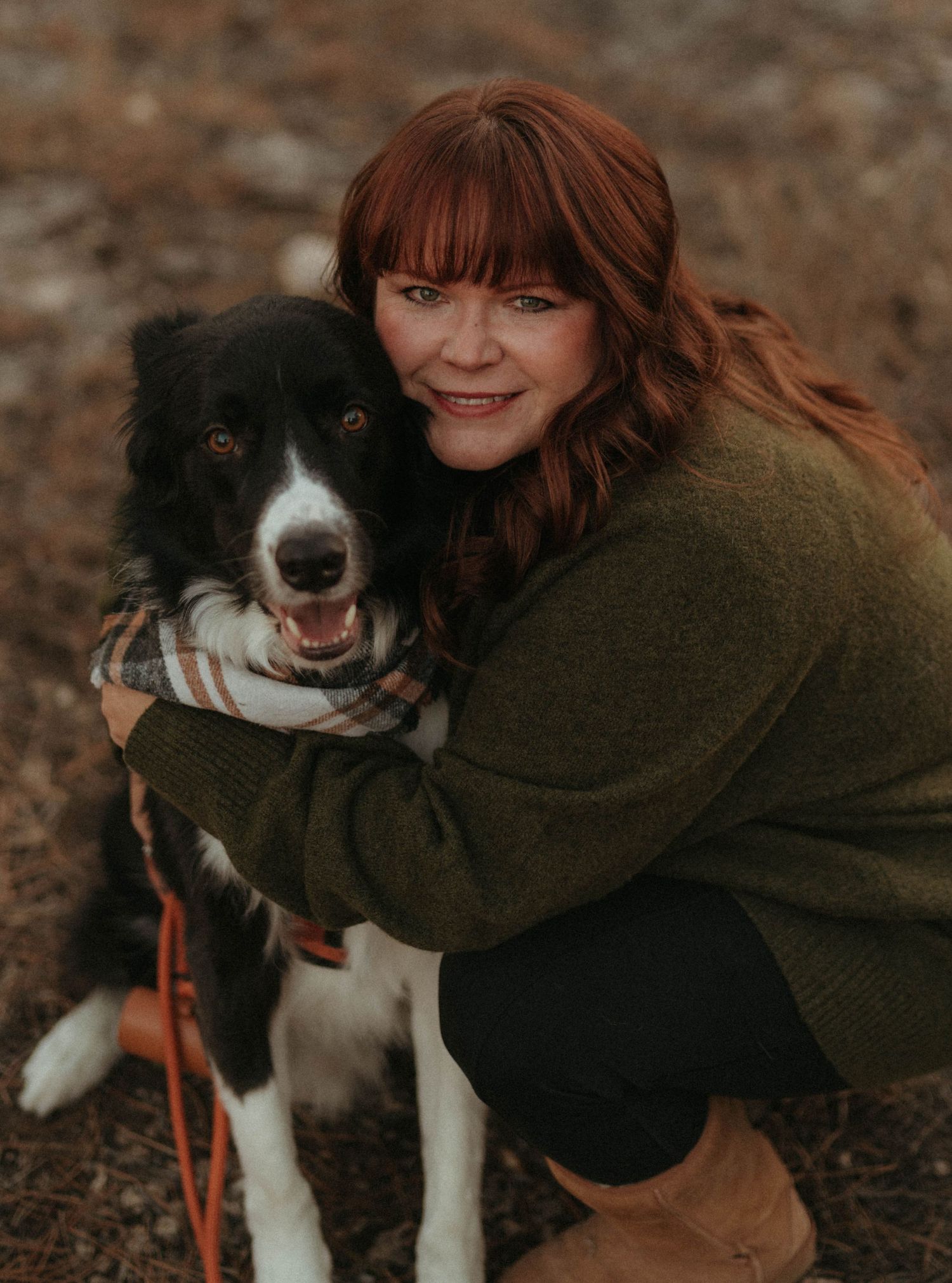 Person in green sweater hugging a happy black and white border collie dog outdoors.