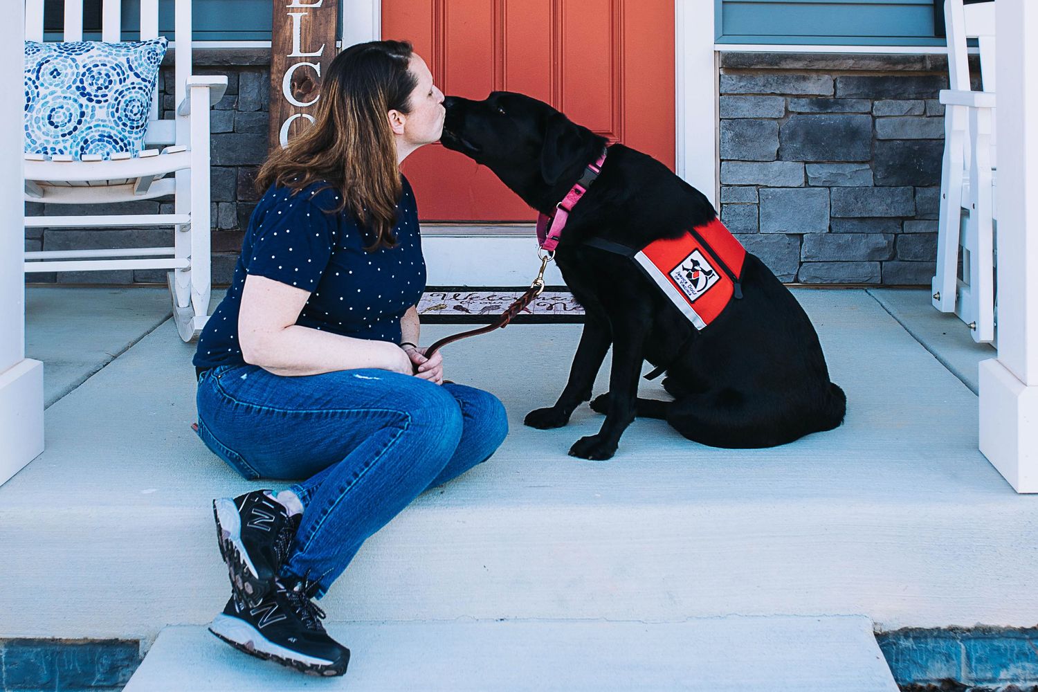 Person sits on a porch with a black dog while petting and bonding with their canine companion.