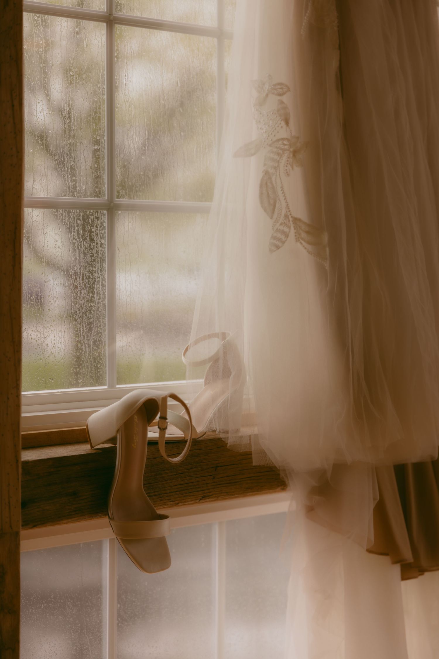 A wedding dress and heels displayed by a window with soft natural lighting creating a dreamy atmosphere.