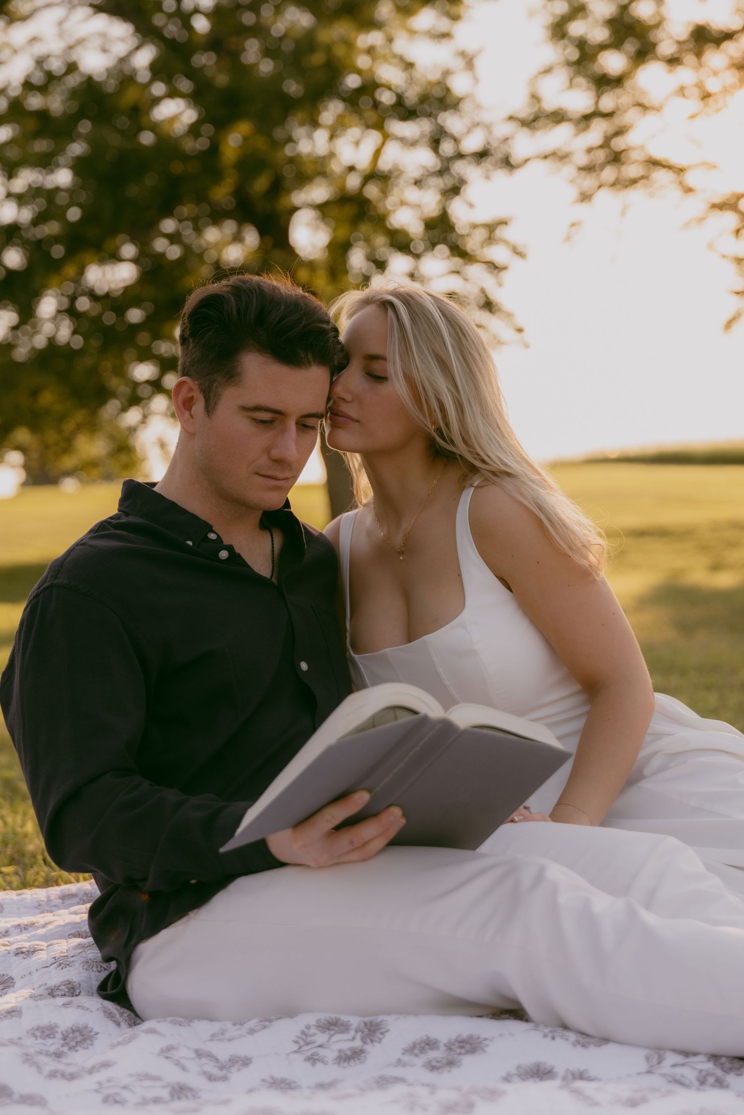 Couple lying together on a blanket in a grassy field during golden hour.