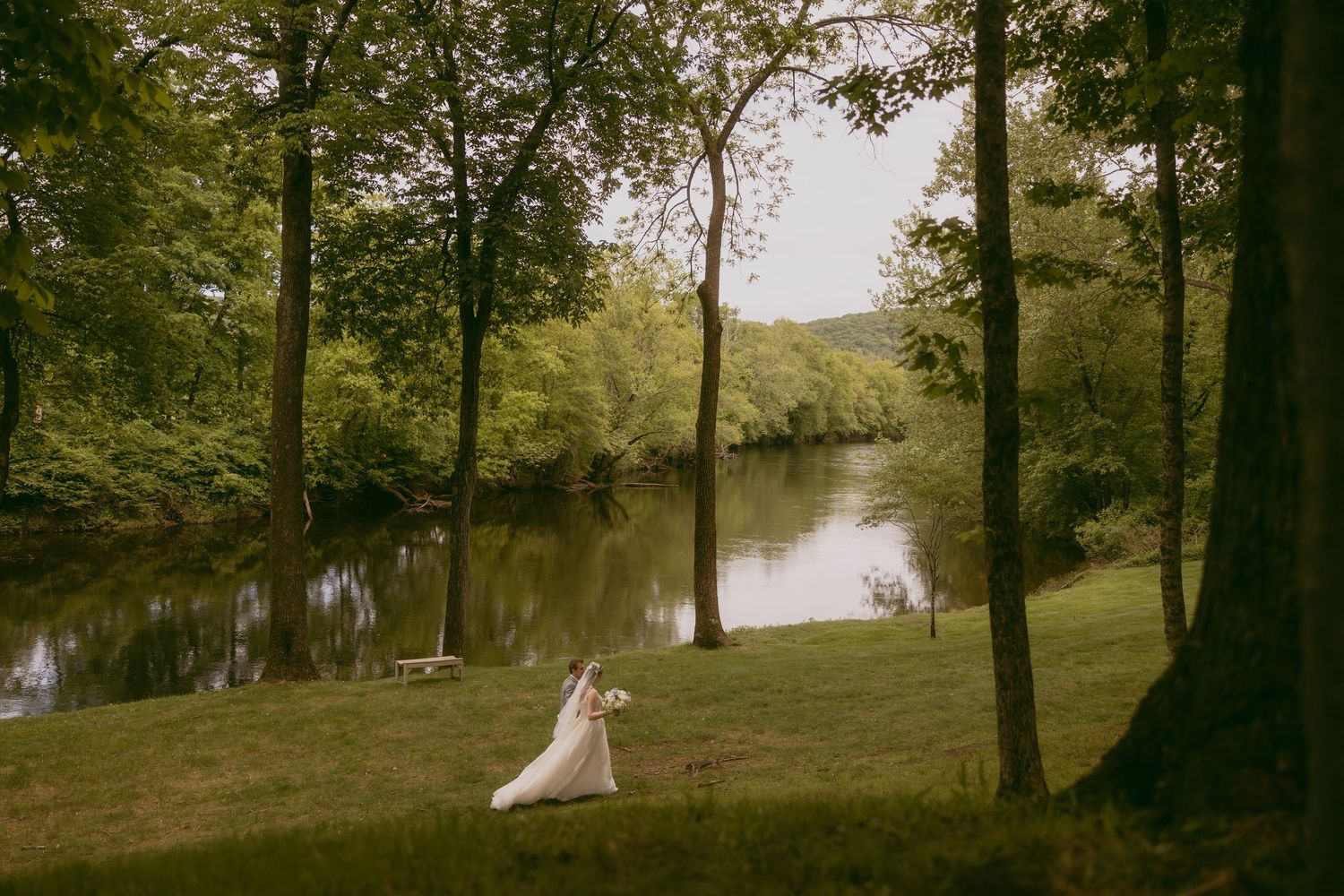 Panoramic lakeside wedding scene with trees and water in golden light.
