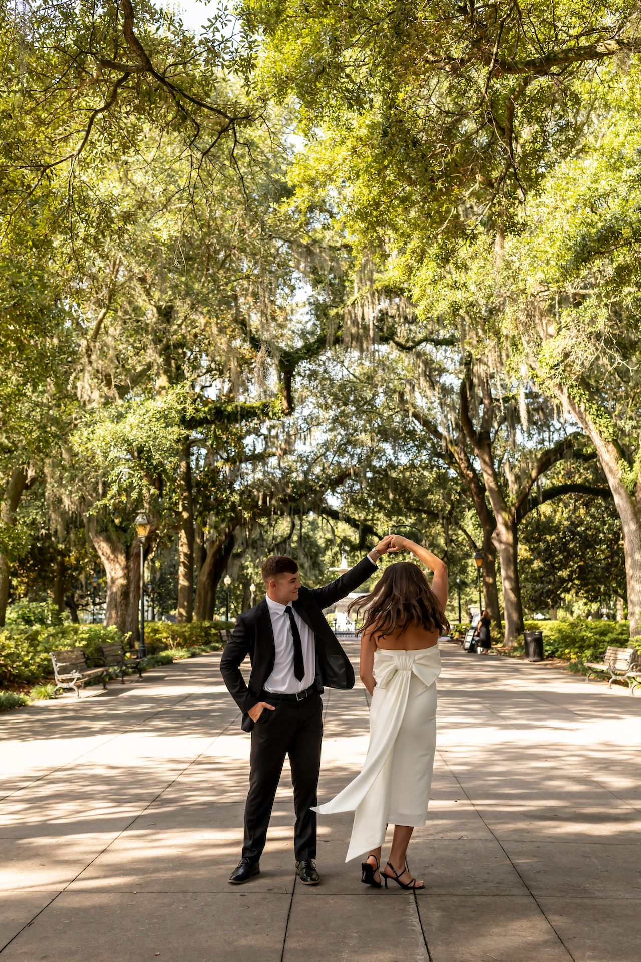 A couple dances together on a sunlit path beneath Spanish moss-draped oak trees in Savannah, Georgia.