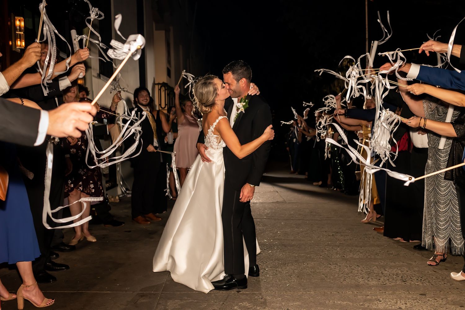 Wedding guests wave sparklers in celebration as newlyweds make their exit from reception venue at night.