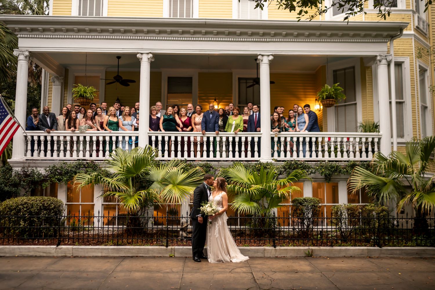 A romantic wedding couple dancing on a wraparound porch at dusk with lighting and palm trees creating an intimate atmosphere.