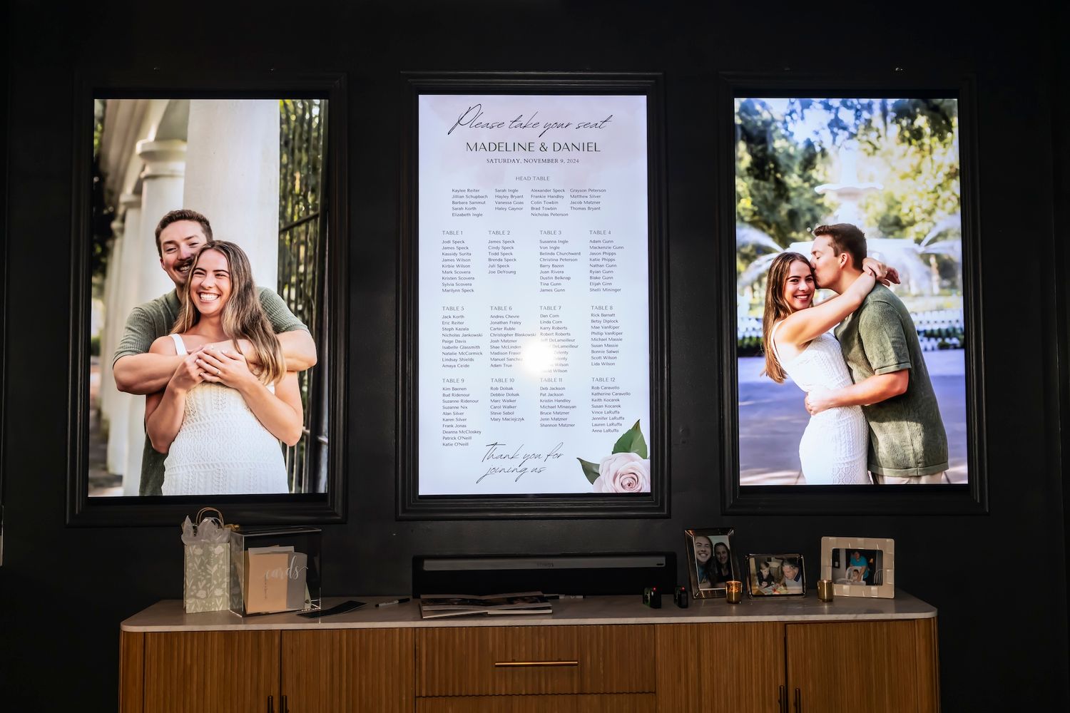 Three framed photos displayed on wooden cabinet showing seating chart in center with romantic couple photos on each side.