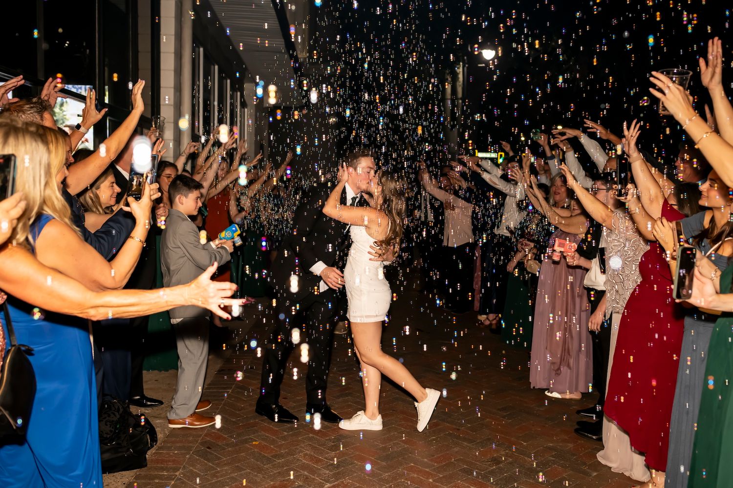 People celebrate and dance as confetti falls at a lively wedding reception during an exit tunnel moment.