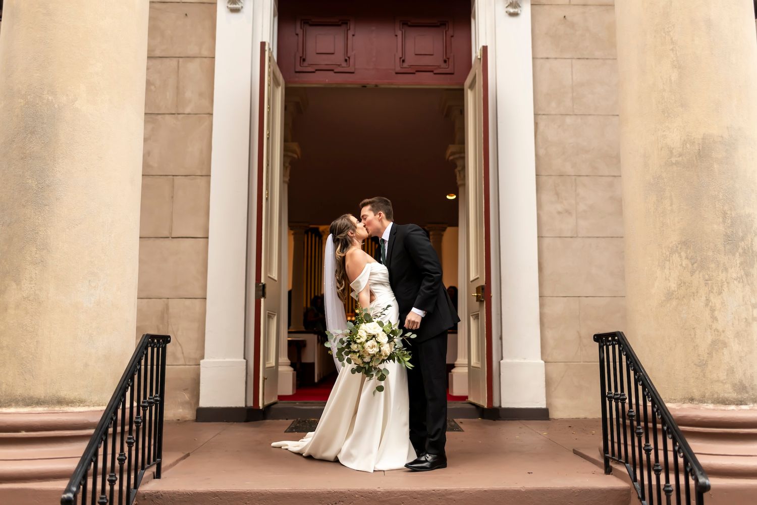 Wedding couple shares a romantic moment in front of columns on building steps.