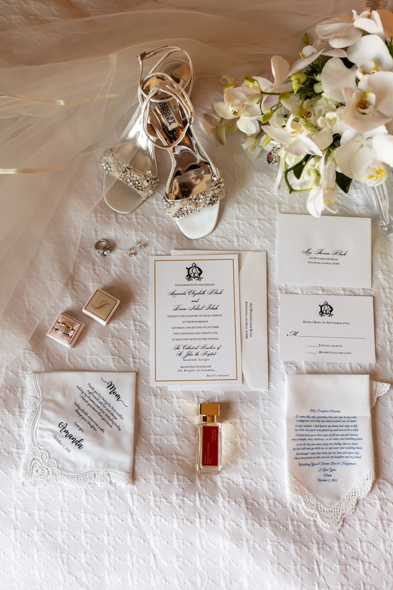 Elegant white wedding invitation suite with floral accents and accessories arranged on textured background.