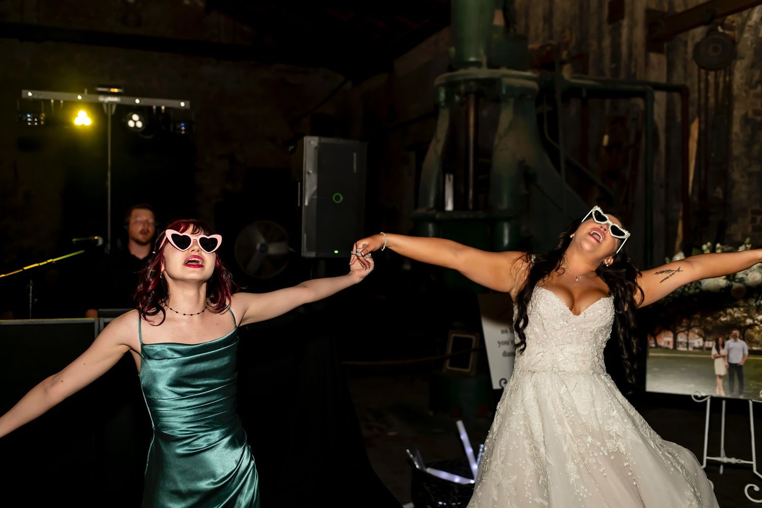 Two wedding guests in formal dresses dance with their arms outstretched on a dark dance floor.