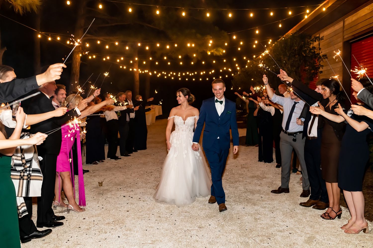 Wedding guests dance beneath glowing string lights at an outdoor evening reception party.