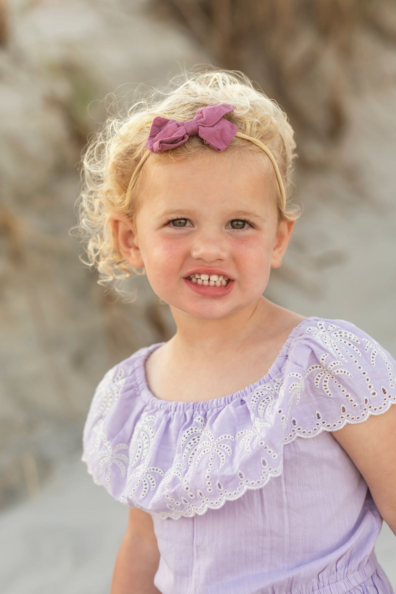 A toddler wearing a lavender eyelet lace dress and a purple hair bow poses outdoors in a series of photos.