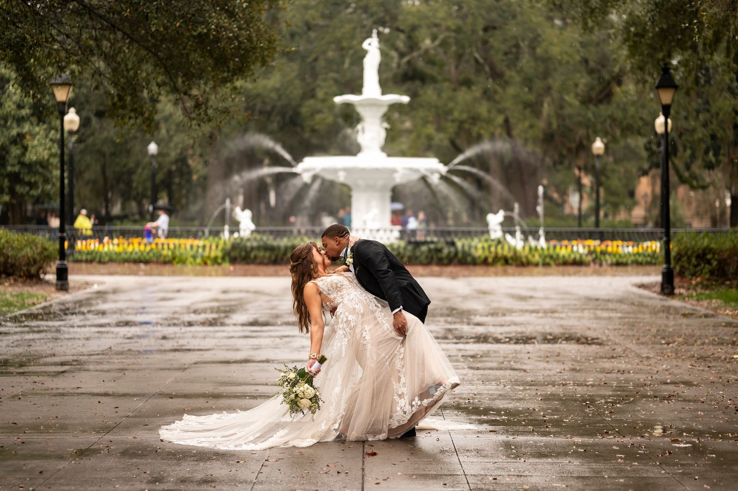 A romantic wedding moment captured in front of Forsyth Park fountain in Savannah during a rainy evening.