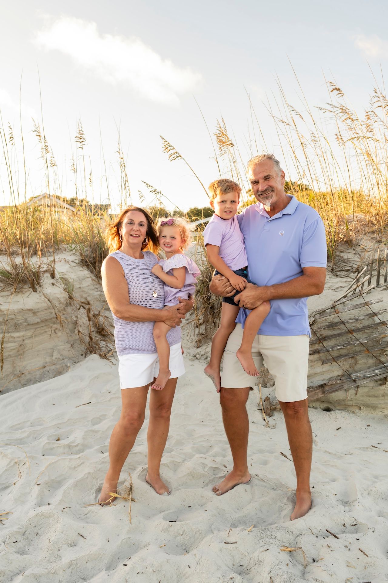 A family stands together on a sandy beach with tall sea oats swaying in the background during golden hour.