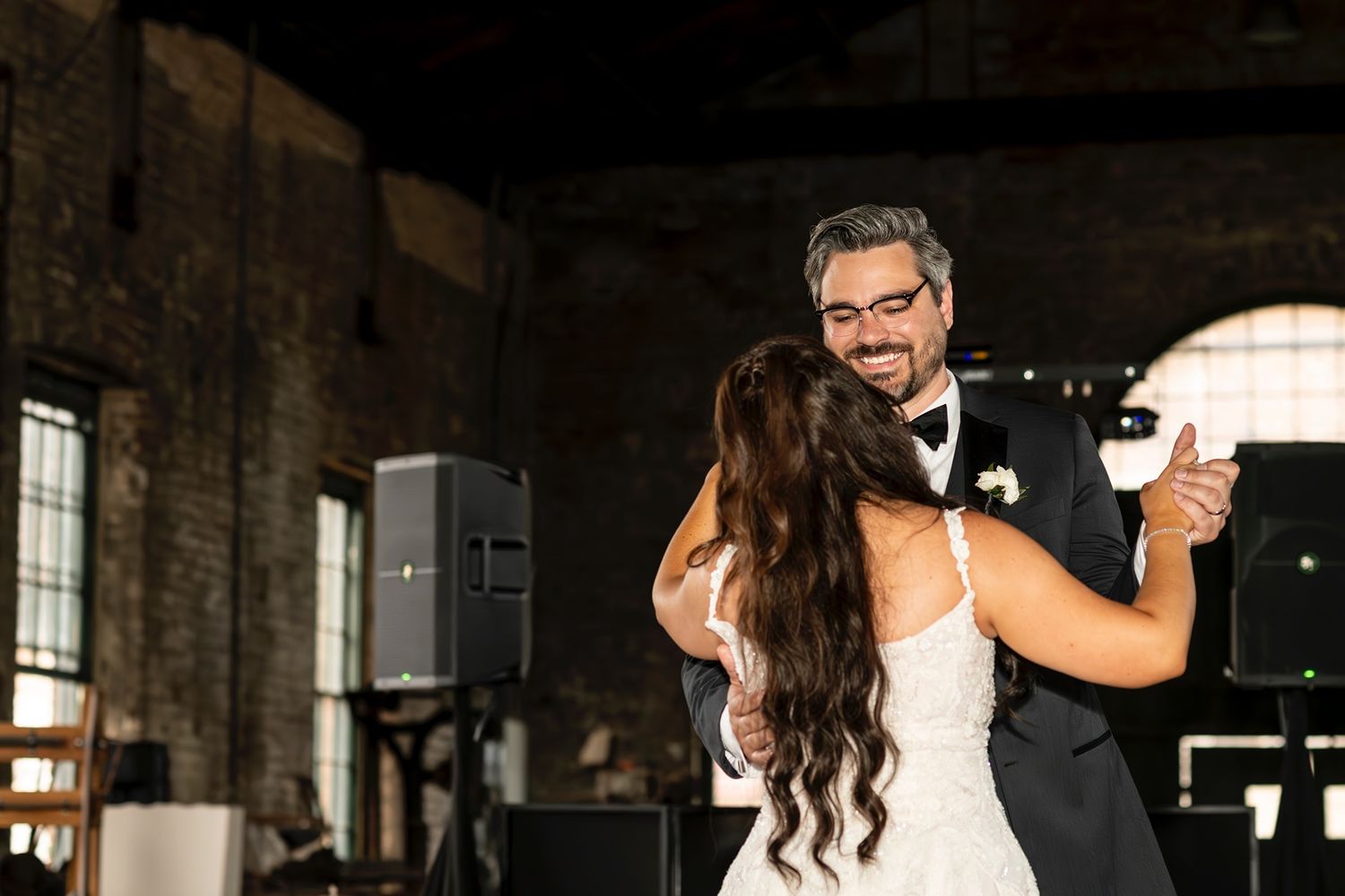 A bride and groom share an intimate first dance together in a rustic industrial venue with exposed brick walls.