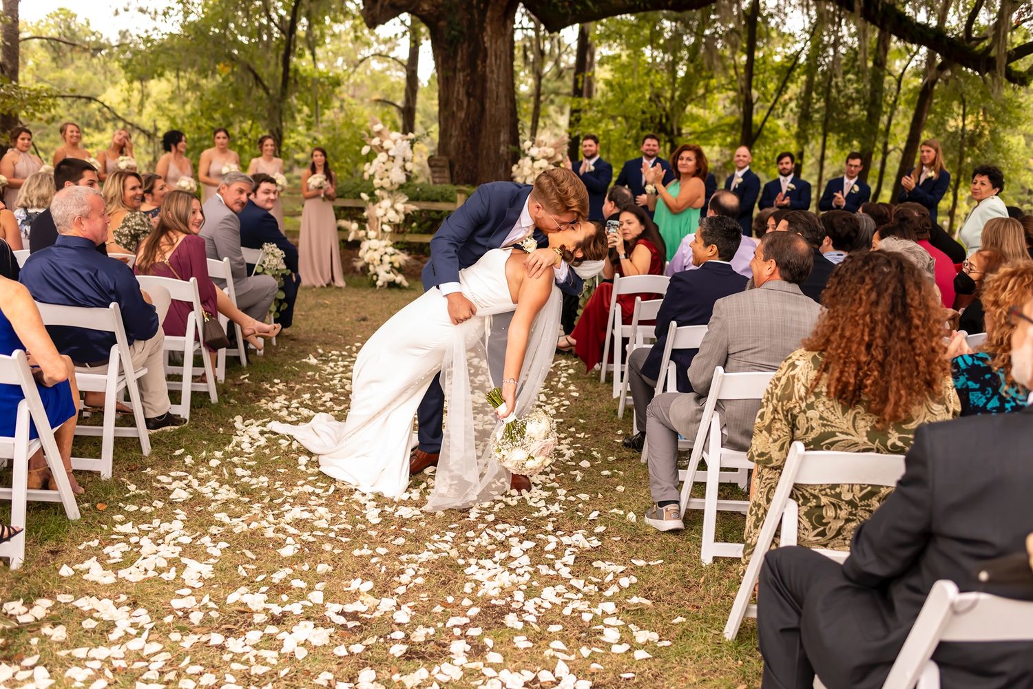 A romantic outdoor wedding ceremony moment with white chairs lined up and flower petals scattered on the ground.