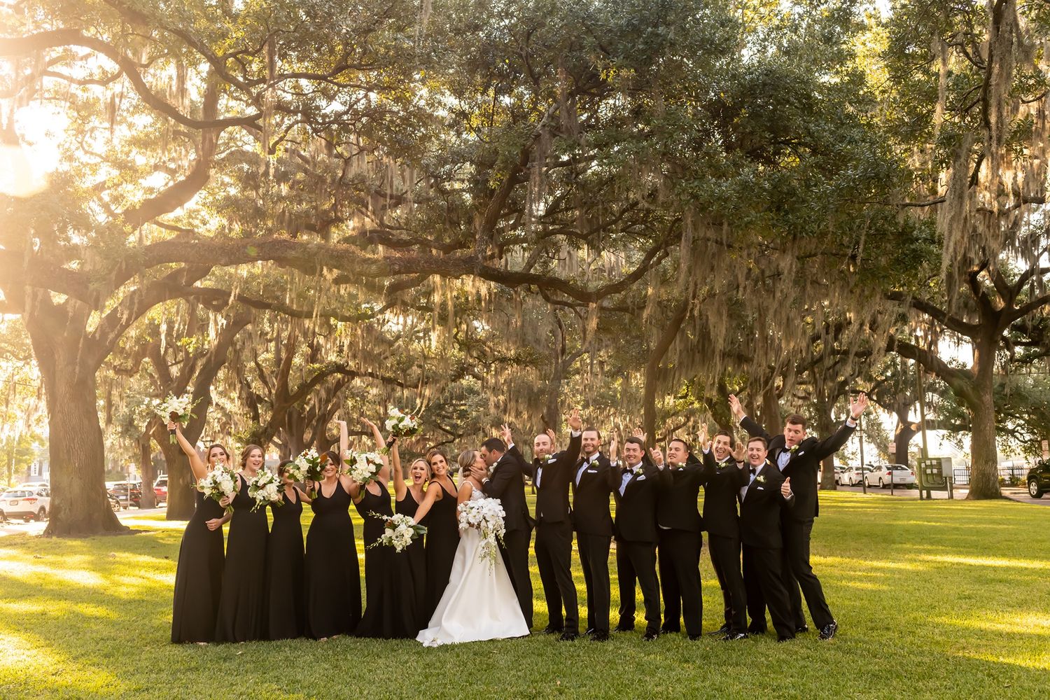 Wedding party poses under Spanish moss-draped oak trees at sunset in a Southern garden setting.
