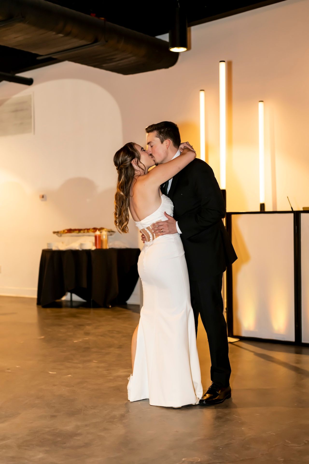 A couple shares a romantic first dance at their modern industrial wedding venue with glowing warm lighting.