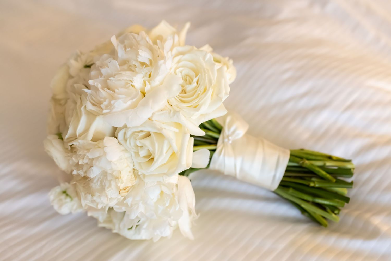 A cascading series of elegant white bridal bouquets with green stems wrapped in ribbon shown from different angles.