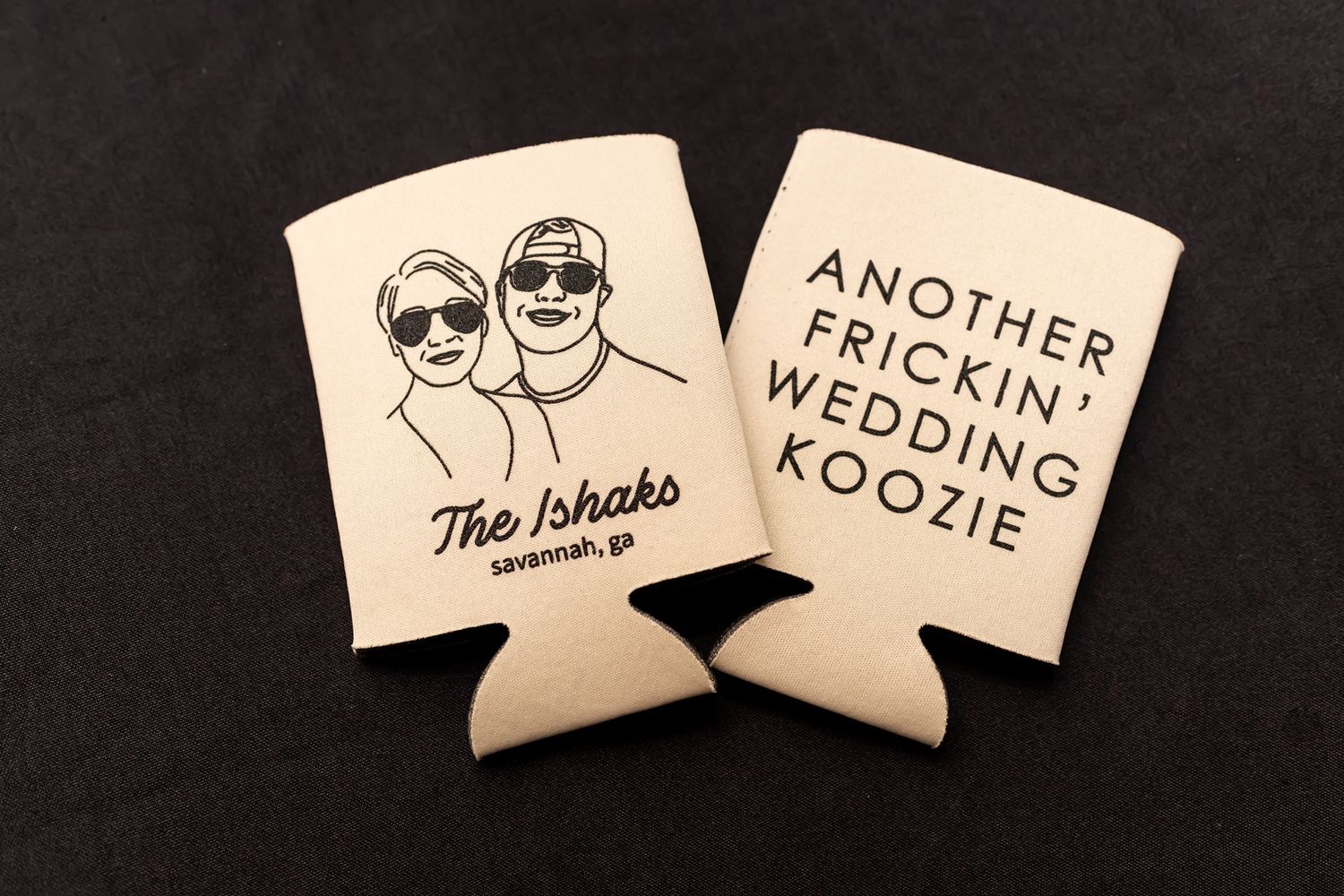 Two white beer koozies with wedding-themed text and cartoon illustrations displayed against a dark background.