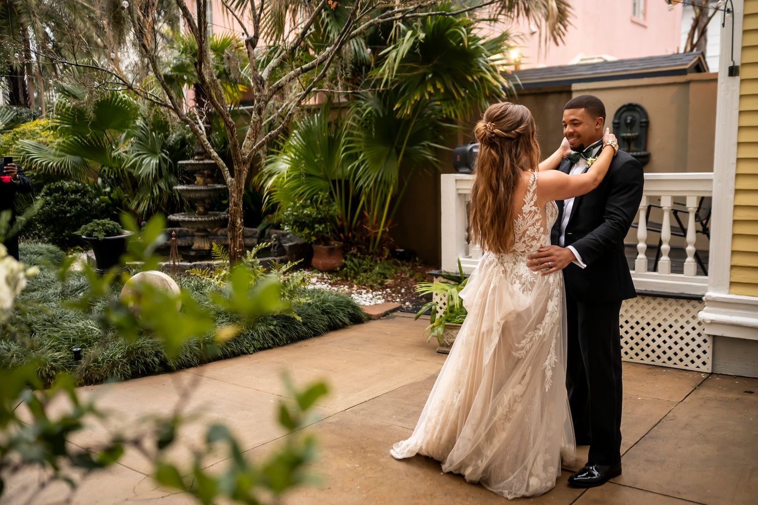 A couple shares their first dance on a romantic garden patio surrounded by lush tropical palms and greenery.