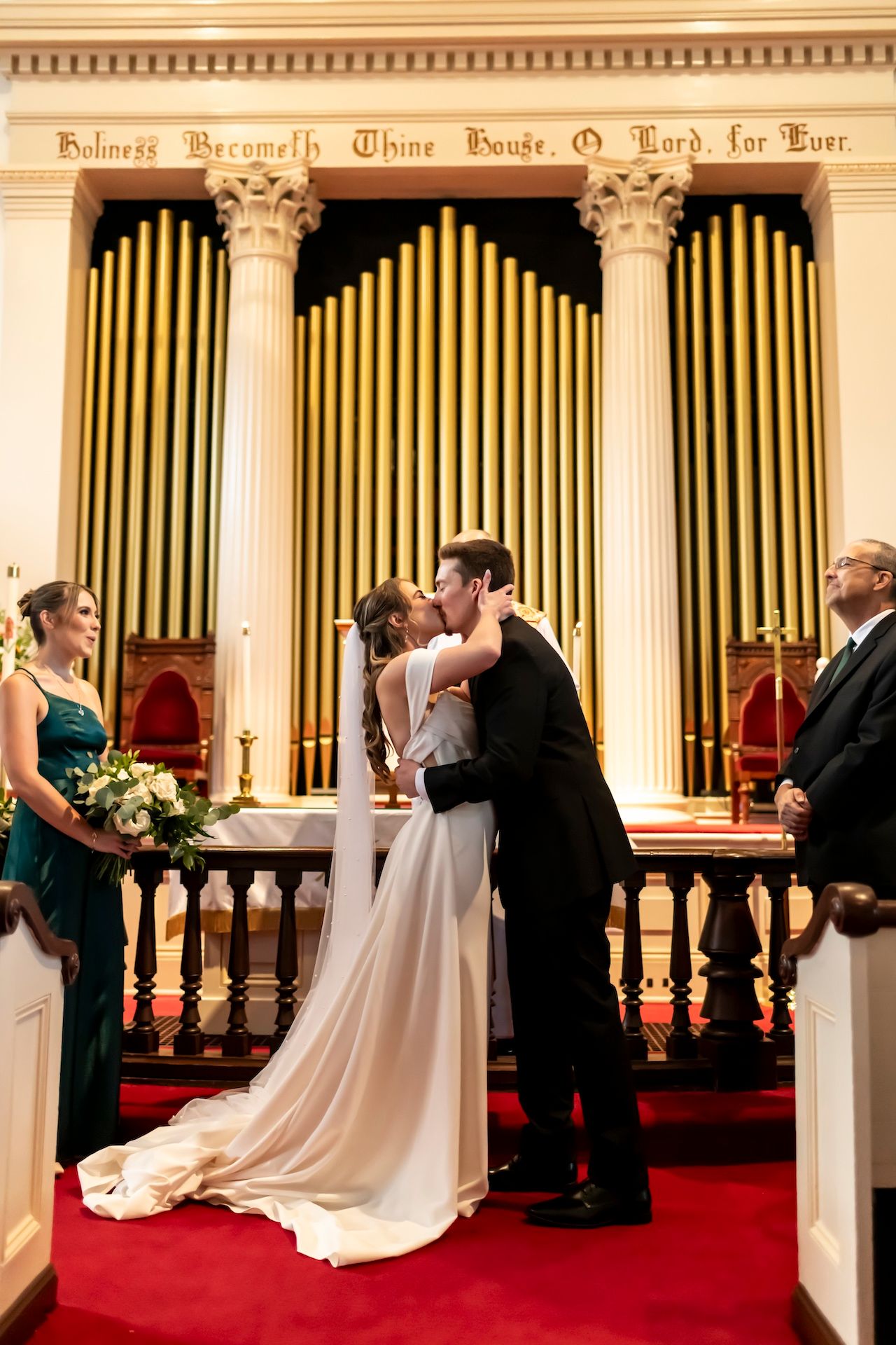 A wedding ceremony takes place inside a historic church with ornate organ pipes and Corinthian columns in the background.