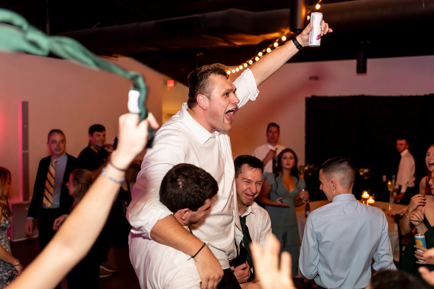 People dancing and having fun at a wedding reception in a dimly lit venue with a DJ performance.