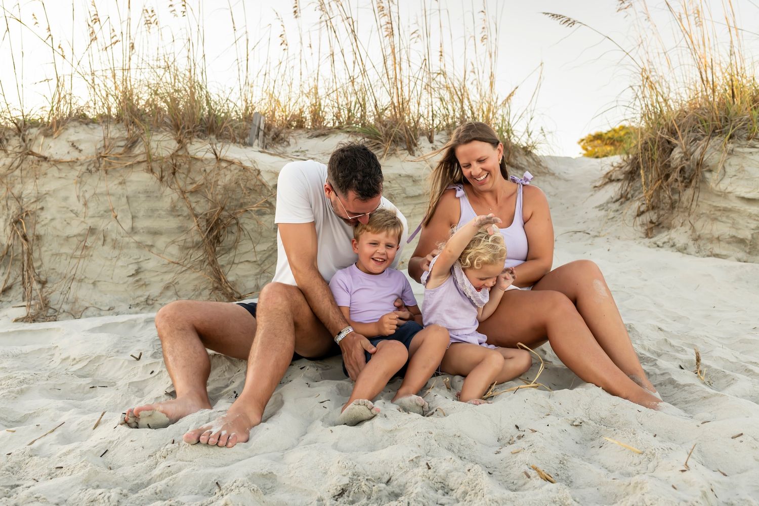 A family relaxes together on sand dunes at the beach during golden hour.