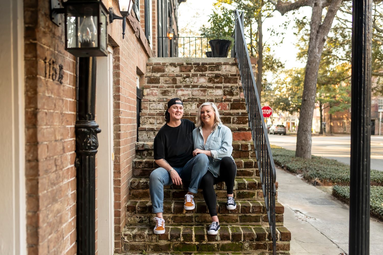 Two people sit casually on brick steps leading to a historic building entrance during autumn.