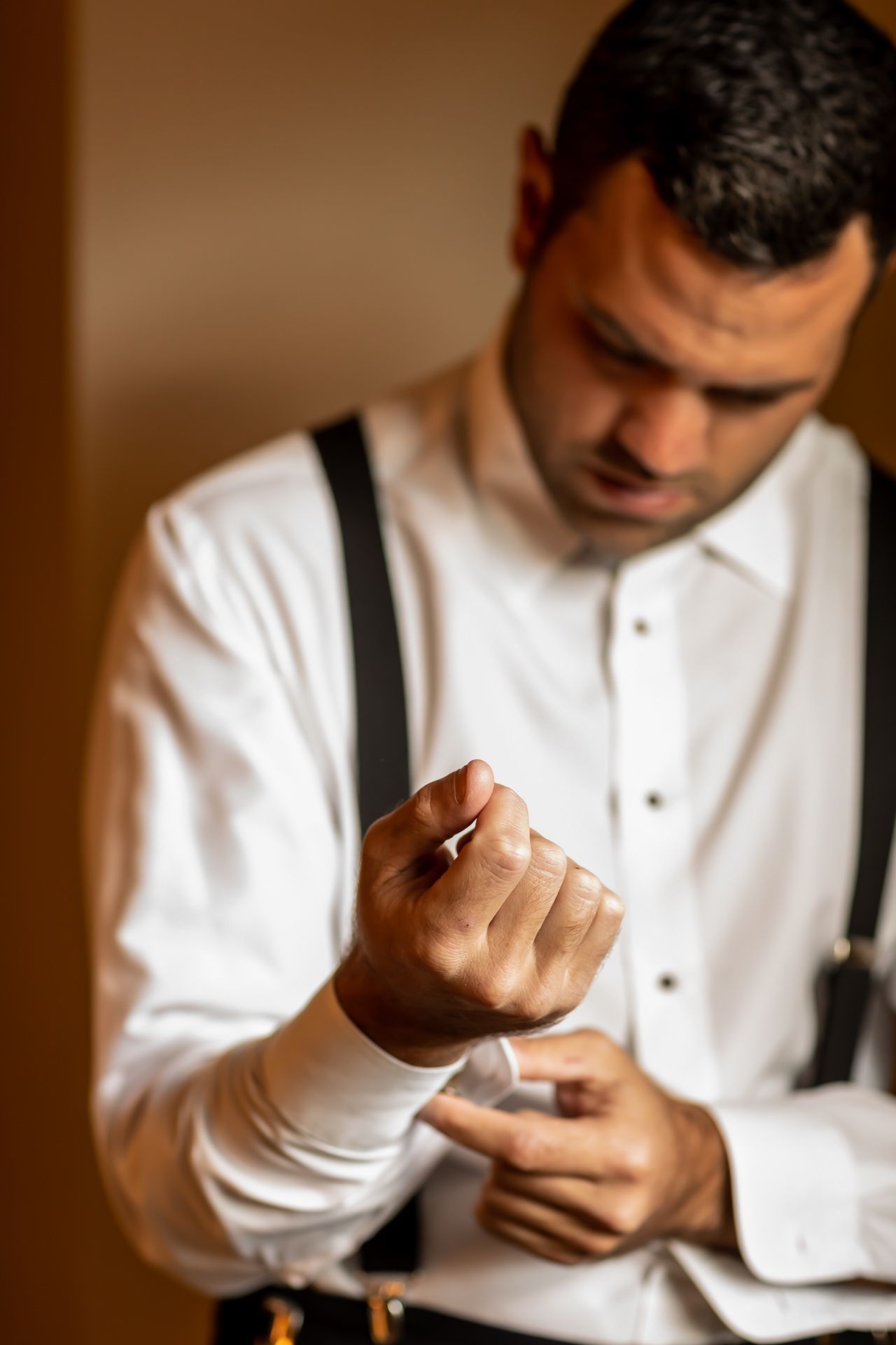 Person in white dress shirt and suspenders adjusts their cuff links in a series of sequential shots.