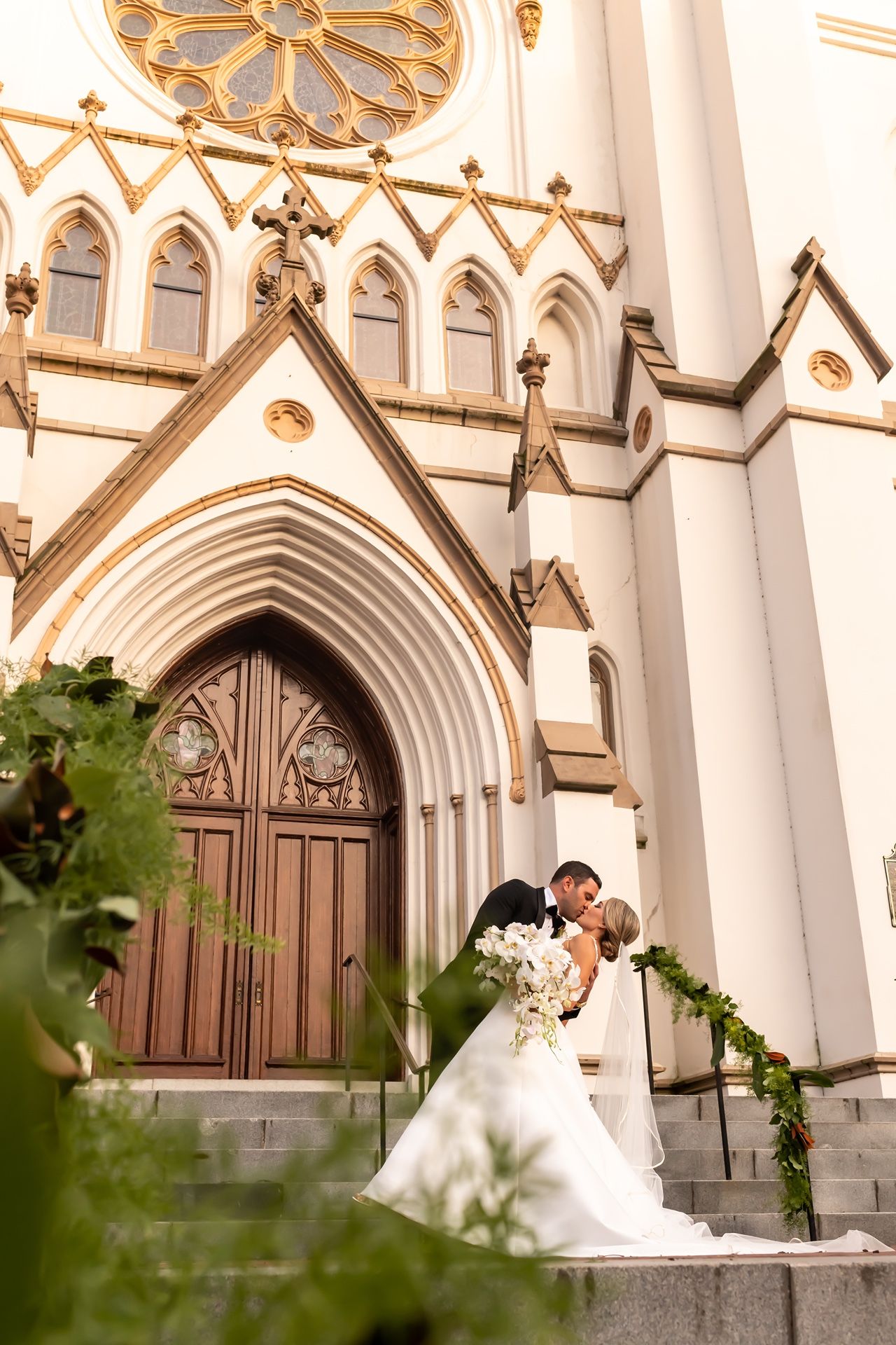 A romantic wedding moment captured on the grand steps of a Gothic cathedral with ornate architectural details.
