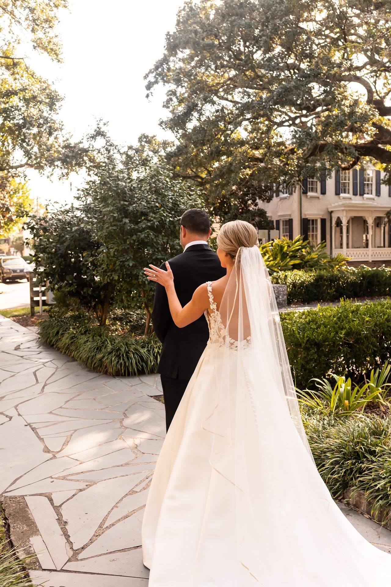 A couple walks along a winding stone path through a garden at sunset while sharing a tender moment in formal attire.