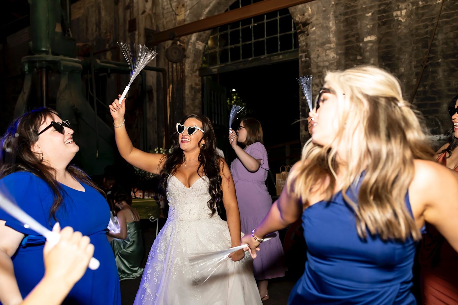 Wedding party guests in blue dresses dance and celebrate with streamers on the dance floor at a reception.