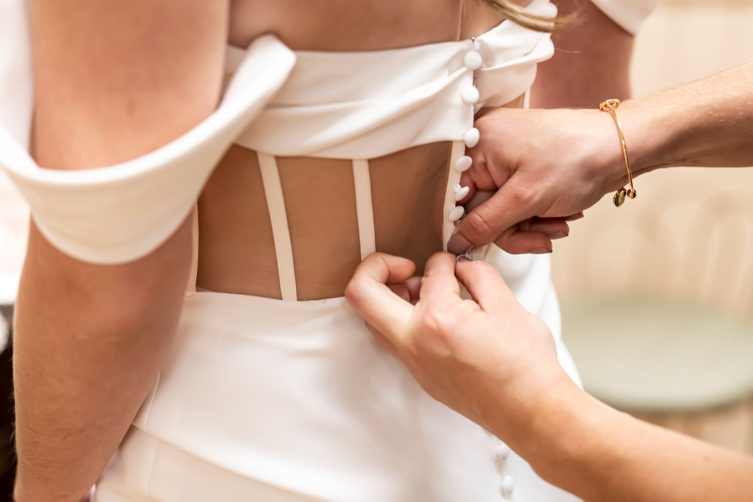 Close-up detail of hands adjusting a white corset dress with delicate lacing and buttons.
