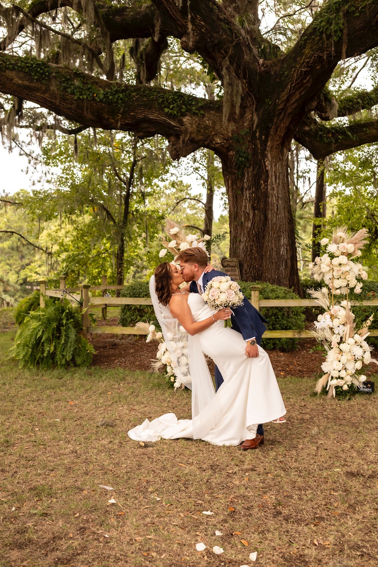 A romantic couple shares tender moments under a majestic old tree in a dreamy outdoor setting.