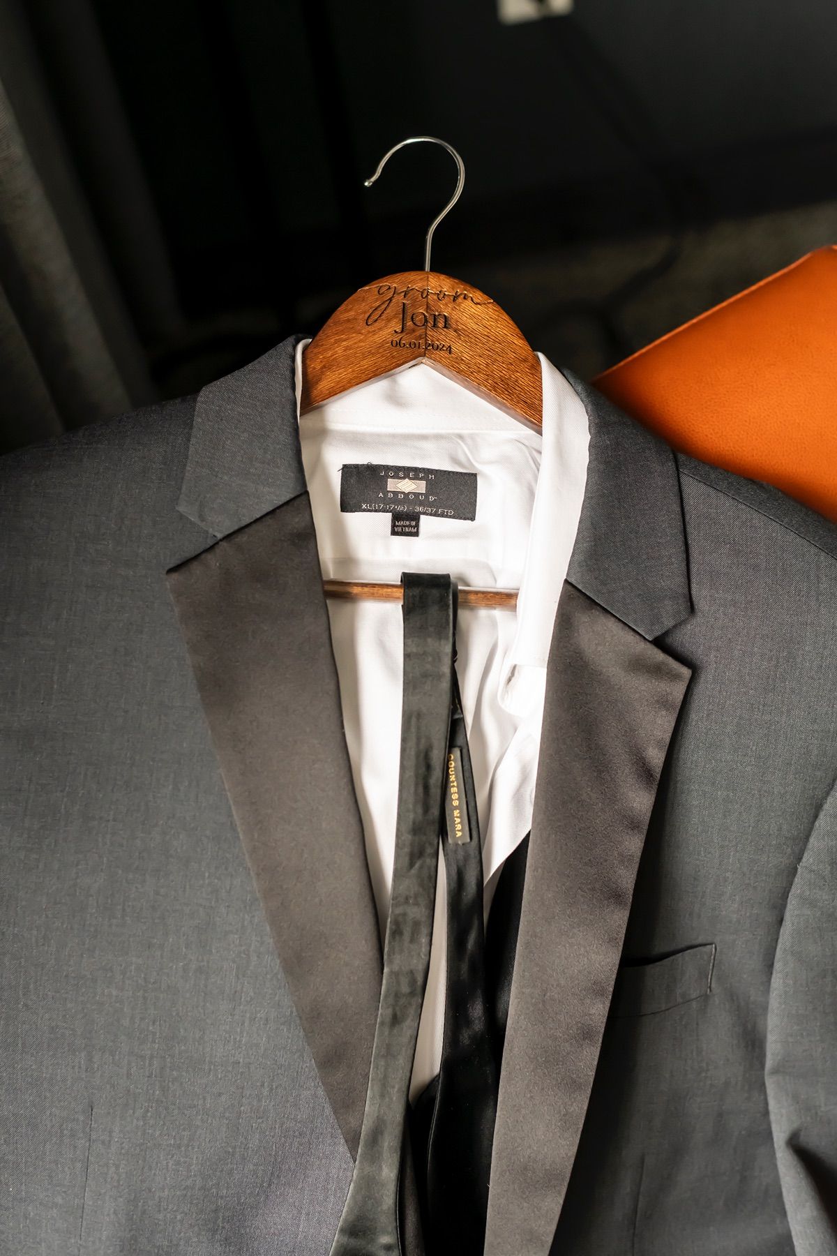A grey suit jacket on a wooden hanger with custom monogram shows crisp white lining against dark background.