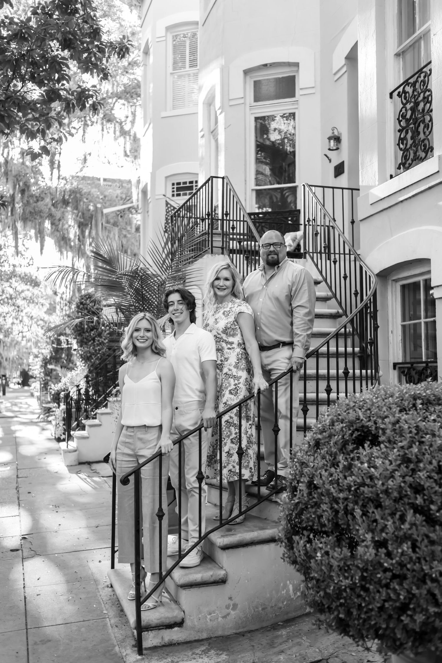 Black and white outdoor portrait showing people arranged on the steps of a historic townhouse with wrought iron railings.